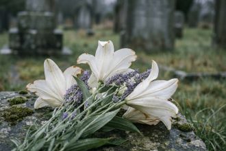 Bouquet de lys blancs et lavande posé sur une pierre tombale dans un cimetière, symbolisant le deuil et le souvenir